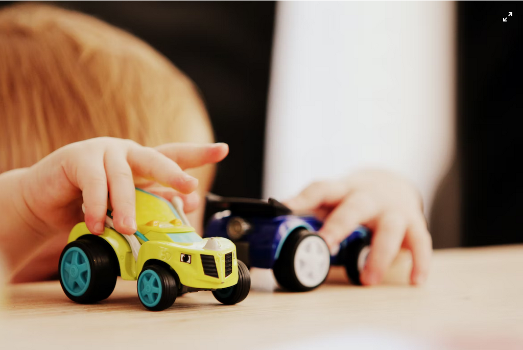"child playing with two assorted-color car plastic toys on brown wooden table"